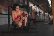 Mujer en ropa deportiva comprobar el tiempo de guardia y sentado entre barras paralelas en el gimnasio - foto de stock