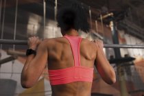 Back view of woman in sportswear doing pull up exercises on horizontal bar in gym — Stock Photo