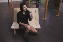 Frau in Sportbekleidung mit Wasserflasche sitzt auf Bank im Fitnessstudio — Stockfoto