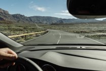 Mano de la cosecha del conductor sosteniendo el volante y moviéndose a las montañas en la carretera rural - foto de stock