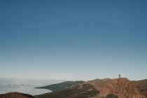 Turista irreconhecível em pé no topo da colina longe em dia sem nuvens — Fotografia de Stock