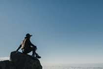 Вид збоку на невпізнавану мандрівну жінку, яка сидить на скелі на схилі пагорба в сонячний день — стокове фото