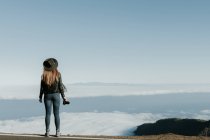 Vista posteriore della donna con macchina fotografica in piedi sulla cima della collina e guardando il paesaggio nuvoloso — Foto stock