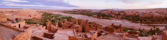 С высоты панорамный вид на старый город с каменными сооружениями вблизи узкой реки между пустыней и красивым небом с облаками в Марракеше, Марокко — стоковое фото