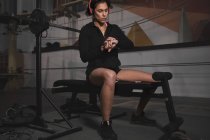 Жінка в спортивному одязі перевіряє час на дивіться і сидить на лавці в спортзалі — стокове фото
