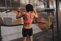 Вид сзади женщины в спортивном костюме, выполняющей упражнения по подтягиванию на турнике в спортзале — стоковое фото