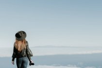 Vista posteriore della donna con macchina fotografica in piedi sulla cima della collina e guardando il paesaggio nuvoloso — Foto stock