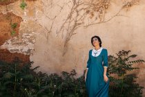 Приваблива арабська жінка в одязі між рослинами біля стіни. — стокове фото