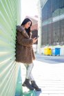 Donna alla moda con smartphone vicino alla parete — Foto stock