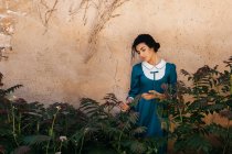 Mulher árabe atraente em vestido entre plantas perto da parede — Fotografia de Stock