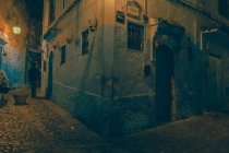Человек, идущий по узкой улице между древними домами и углом каменного здания вечером в Марракеше, Марокко — стоковое фото