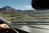 Mano de la cosecha del conductor sosteniendo el volante y moviéndose a las montañas en la carretera rural - foto de stock