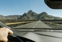 Crop hand du conducteur tenant le volant et se déplaçant vers les montagnes sur la route rurale — Photo de stock