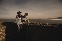 Вид збоку на стильну елегантну пару біля скель на узбережжі біля моря і чудове небо — стокове фото