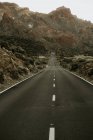 Perspective view to asphalt road in dry land leading to mountains — Stock Photo