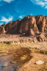 Pintoresca vista del río que corre cerca de acantilados rocosos en el desierto y el cielo azul en Marrakech, Marruecos - foto de stock