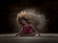 Mujer joven bailando y usando polvo en la oscuridad - foto de stock