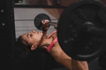 Mujer en ropa deportiva haciendo ejercicios con barras en press de banca en el gimnasio - foto de stock