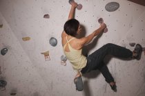 Vue arrière de la femme en tenue de sport s'entraînant sur un mur d'escalade avec des cales dans la salle de gym — Photo de stock