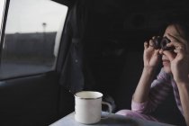 Женщина смотрит через шоколадное печенье и сидит в автомобиле рядом с кружку с ложкой на столе — стоковое фото