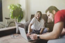 Sonriente joven hombre y mujer sentado en el sofá y la computadora portátil de navegación en la sala de estar - foto de stock