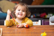 Маленькая девочка рисует яйцо за столом — стоковое фото