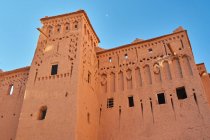 Desde abajo fachada de construcción rocosa en la ciudad vieja y cielo azul en Marrakech, Marruecos - foto de stock