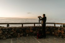 Vista laterale del fotografo maschio irriconoscibile in piedi con fotocamera e scattare scatti di vista dalla collina — Foto stock