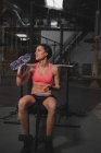 Femme en vêtements de sport avec bouteille d'eau assise sur le banc dans la salle de gym — Photo de stock