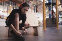 Vista lateral de mujer en ropa deportiva con auriculares escuchando música y zapato de cordones en gimnasio - foto de stock