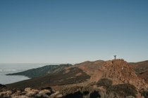 Touriste méconnaissable debout sur le sommet de la colline de loin dans une journée sans nuages — Photo de stock