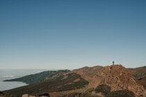 Touriste méconnaissable debout sur le sommet de la colline de loin dans une journée sans nuages — Photo de stock