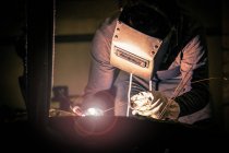 Человек в сварочном шлеме работает с металлопродуктом на маленьком литейном заводе — стоковое фото