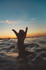 Рука крупным планом человека показывает знак шака над поверхностью воды с рябью и голубым небом вечером на бали, Индонезия — стоковое фото