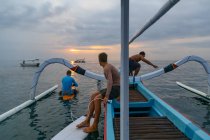 Side view of males jumping from shallop in waving sea and cloudy sky in evening on Bali, Indonesia — Stock Photo