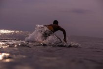 Vista posteriore del maschio galleggiante su tavola da surf tra acqua di mare e cielo nuvoloso a Bali, Indonesia — Foto stock