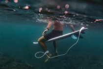 Вид сбоку мужчины, плавающего на доске для серфинга в лазурной морской воде на острове Бали, Индонезия — стоковое фото