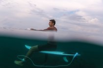 Seitenansicht eines Mannes, der auf einem Surfbrett im azurblauen Wasser des Meeres auf Bali, Indonesien schwimmt — Stockfoto