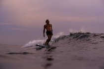 Surf maschile tra acqua di mare ondulata con spruzzi e cielo nuvoloso in serata a Bali, Indonesia — Foto stock