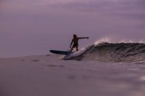 Мужской серфинг между волнистой морской водой с брызгами и облачным небом вечером на Бали, Индонезия — стоковое фото