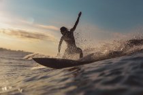 Male surfing between waving water of sea with splashes and cloudy sky in evening on Bali, Indonesia — Stock Photo