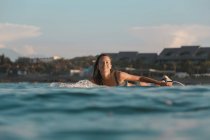 Seitenansicht einer fröhlichen Frau, die auf einem Surfbrett zwischen Meer und blauem Himmel auf Bali, Indonesien, schwimmt — Stockfoto