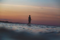 Side view of silhouette of male with paddle on surf board between water of sea and sky in evening on Bali, Indonesia — Stock Photo
