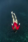 Dall'alto femmina in costume da bagno rosso che si tuffa in acqua azzurra di mare su Bali, Indonesia — Foto stock