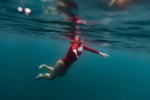 Side view of female in red swimsuit diving in blue water of sea on Bali, Indonesia — Stock Photo