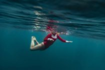 Вид сбоку женщины в красном купальнике, ныряющей в синюю морскую воду на Бали, Индонезия — стоковое фото