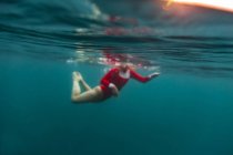 Вид сбоку женщины в красном купальнике, ныряющей в синюю морскую воду на Бали, Индонезия — стоковое фото