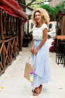 Retrato de la alegre y elegante joven negra con el pelo rizado y el bolso de pie en la calle en México - foto de stock