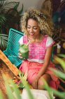 Щаслива чорна молода жінка тримає склянку струсу і сидить біля дерев'яного столу з мискою овочів в кафе — стокове фото