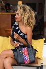 Stylish black young woman with curly hair and handbag in dress sitting on bench — Stock Photo